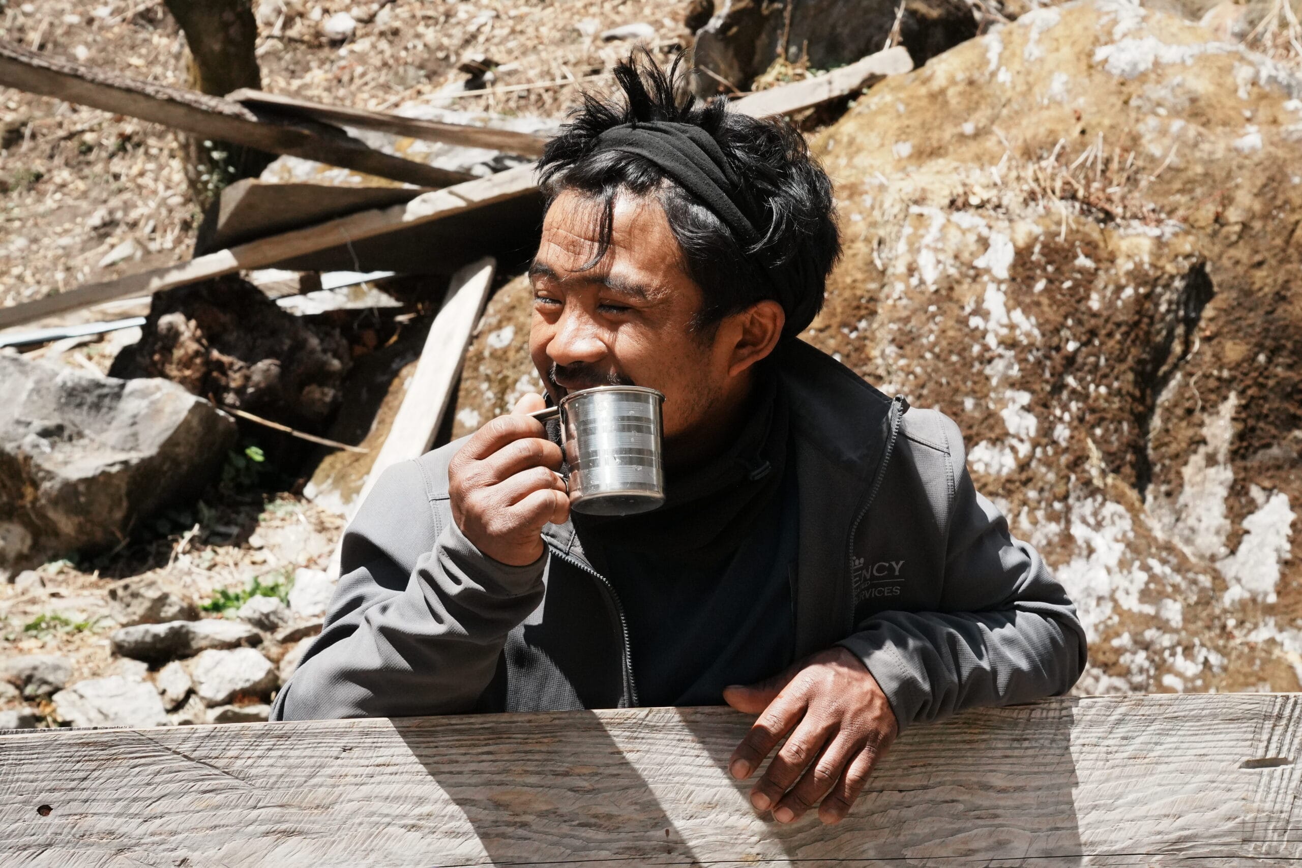 Guide népalais souriant buvant du thé dans une tasse en métal pendant un trek